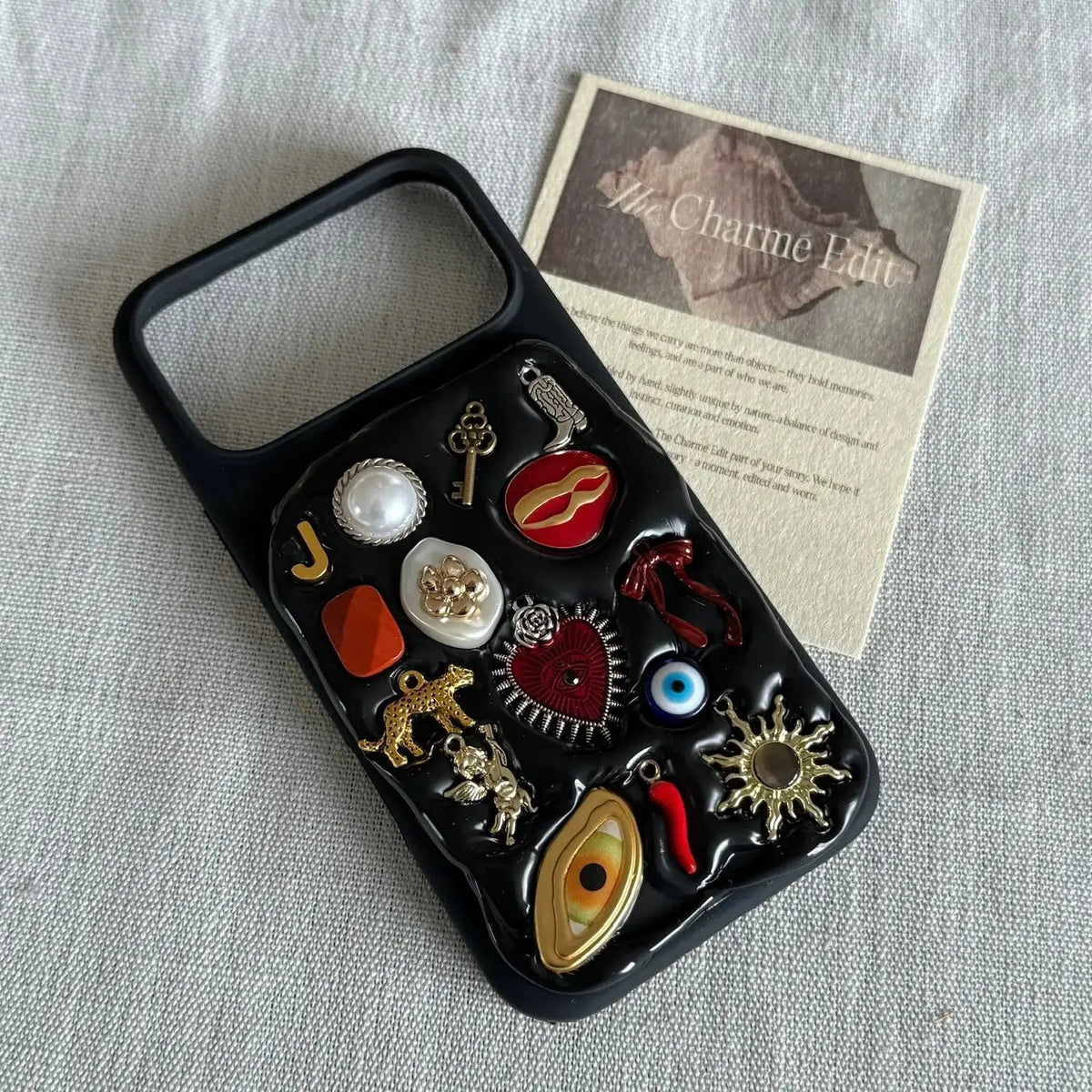 The Charmé Edit custom charm phone case on a linen background with brand card