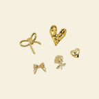 Set of gold charms including bow and heart designs on a beige background
