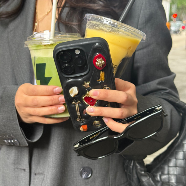 Person holding a phone with a decorative case, two drinks, and sunglasses.