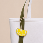 The Amalfi Lemon hand-beaded lemon slice bag charm tied to a white tote