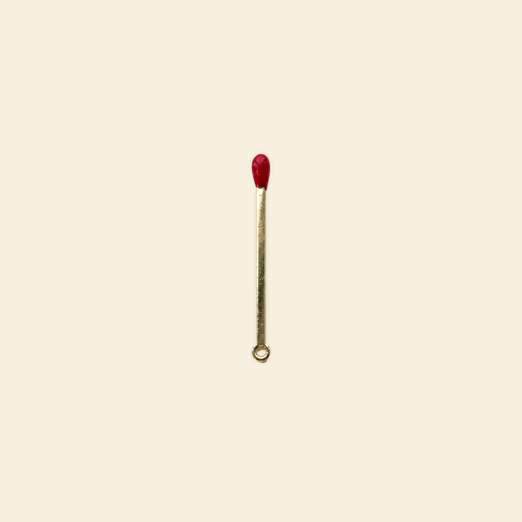 gold matchstick charm on a solid #f7f0df background
