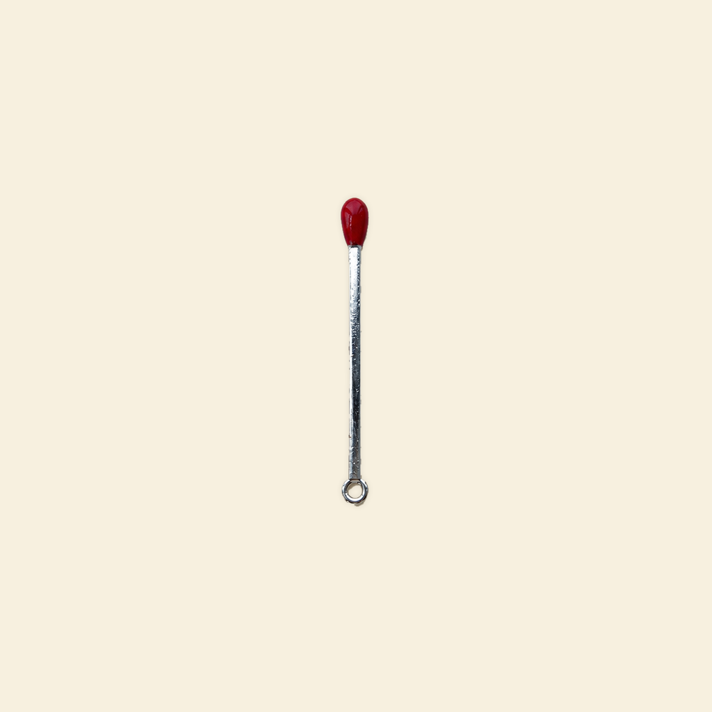 silver matchstick charm on a solid #f7f0df background