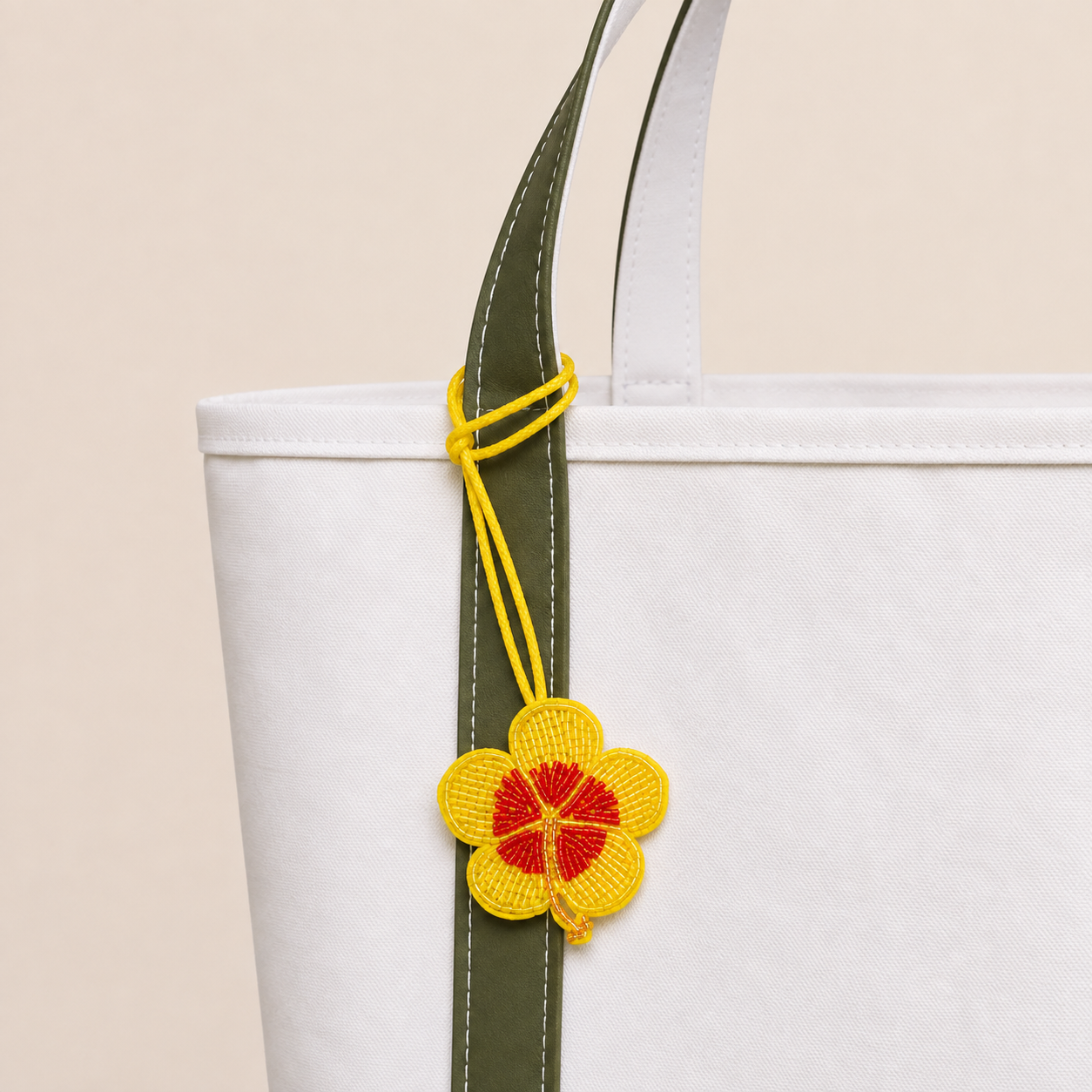 The Soleil Bloom hand-beaded flower bag charm tied to a white tote